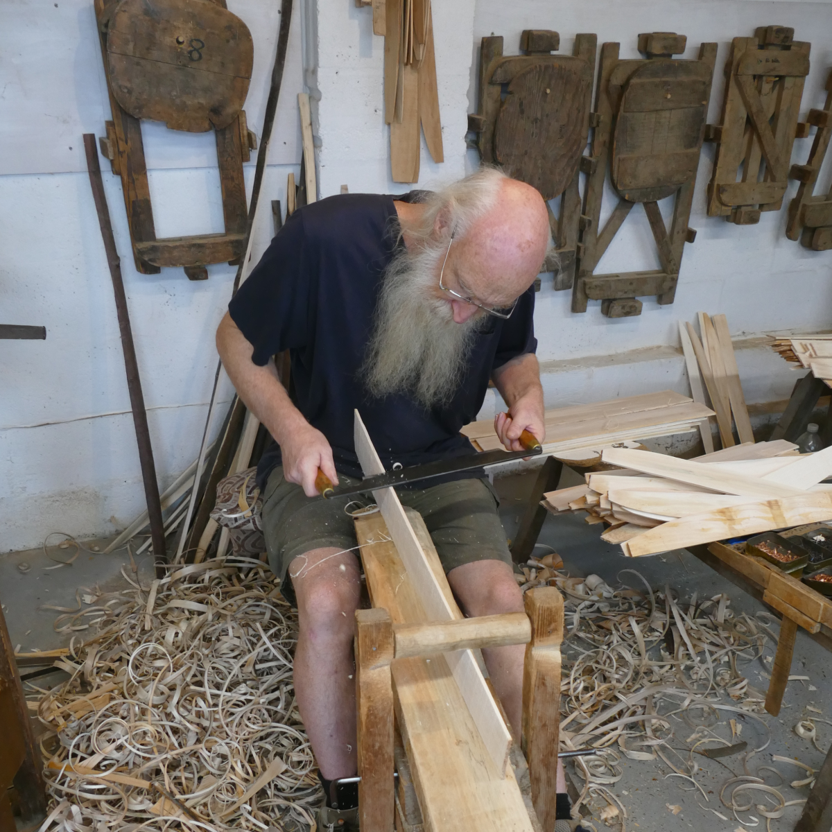 Craftsperson hand-shaping a wooden trug at The Truggery, Herstmonceux, surrounded by tools, shavings and trug moulds.